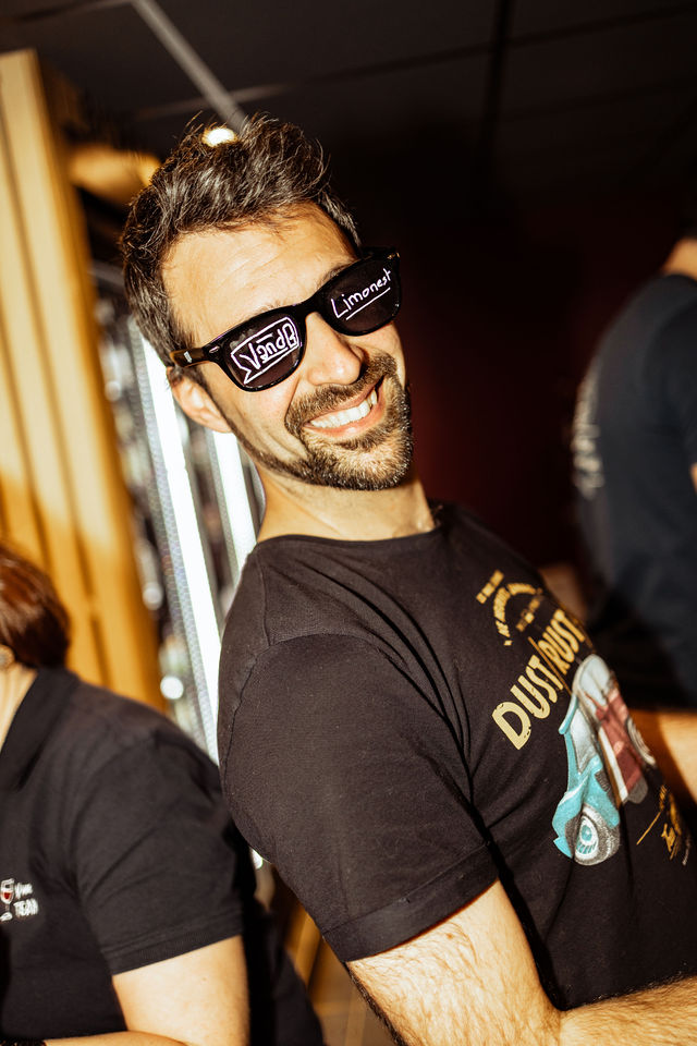 Homme souriant portant des lunettes noires avec texte et t-shirt vintage