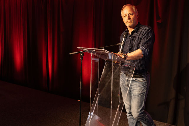 Homme en chemise debout à un pupitre sur scène éclairée en rouge
