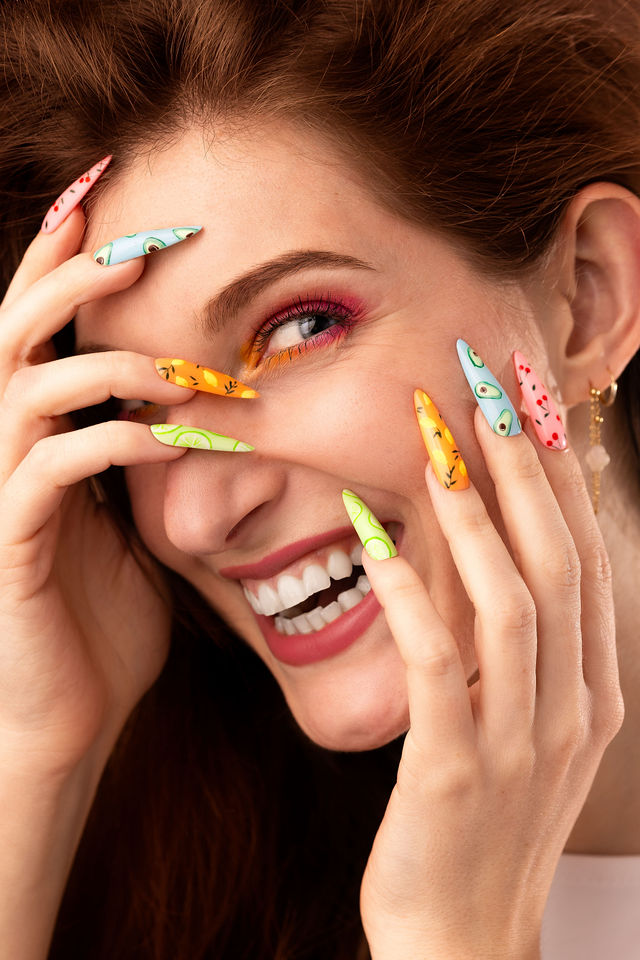 Femme souriante avec maquillage coloré et ongles à motifs fruits
