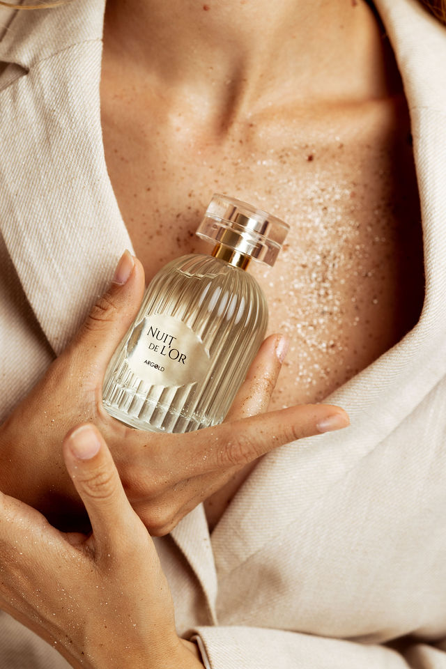 Parfum Nuit de l’Or Argold tenu contre une peau pailletée