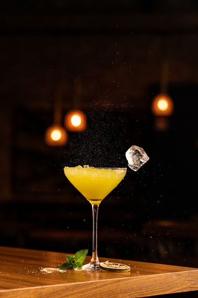 Cocktail jaune dans verre à martini avec glaçon en chute et zeste de citron
