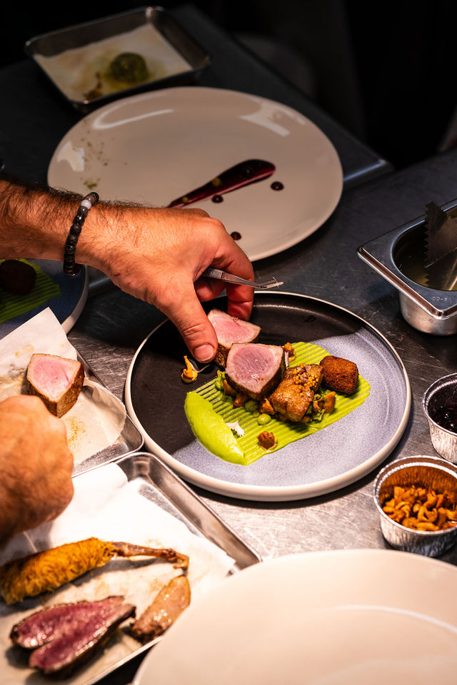 Main dressant une assiette gastronomique avec purée verte et viande, cuisine professionnelle