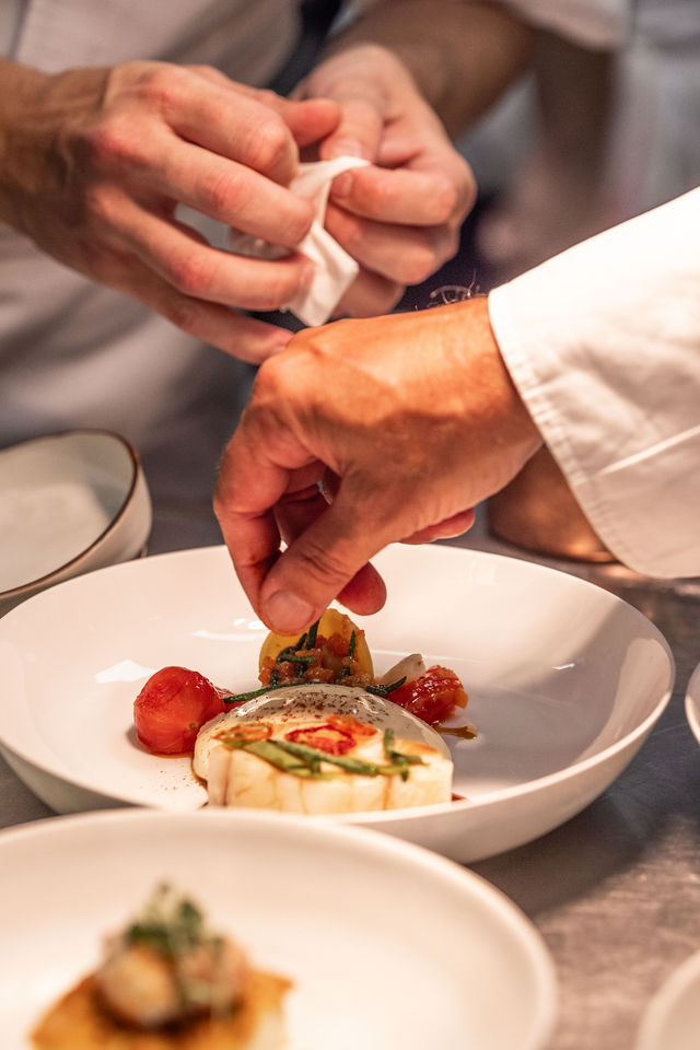 Dressage d’une assiette blanche en cuisine avec mains de chefs en action