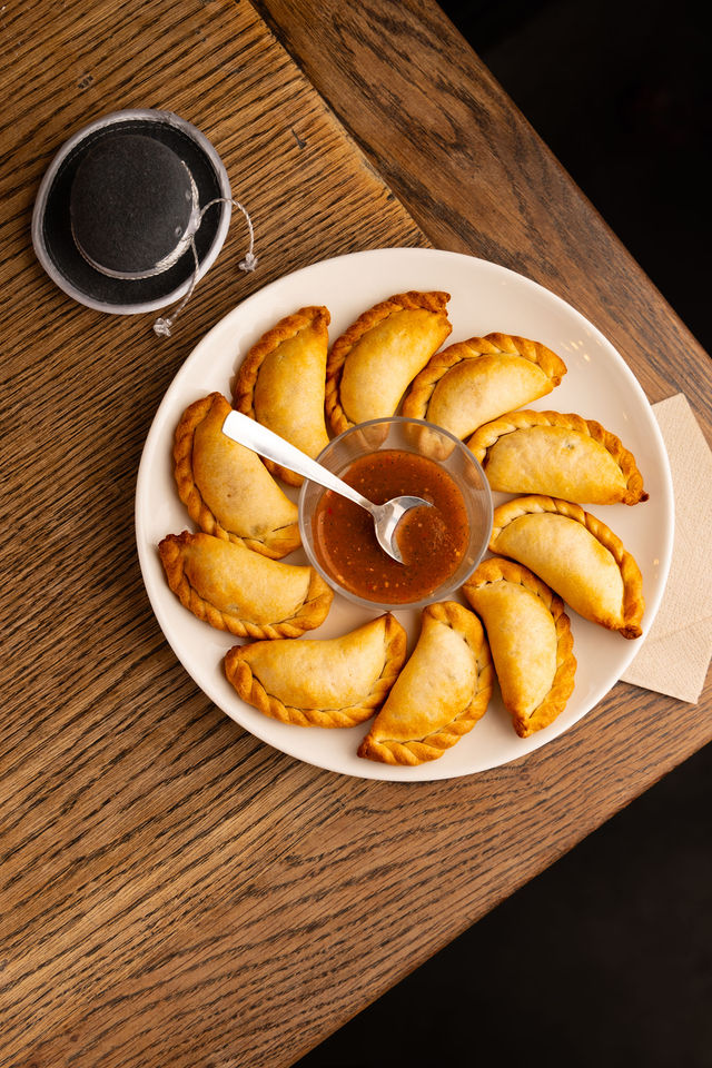 Assiette d’empanadas disposés en cercle avec sauce au centre, sur table en bois