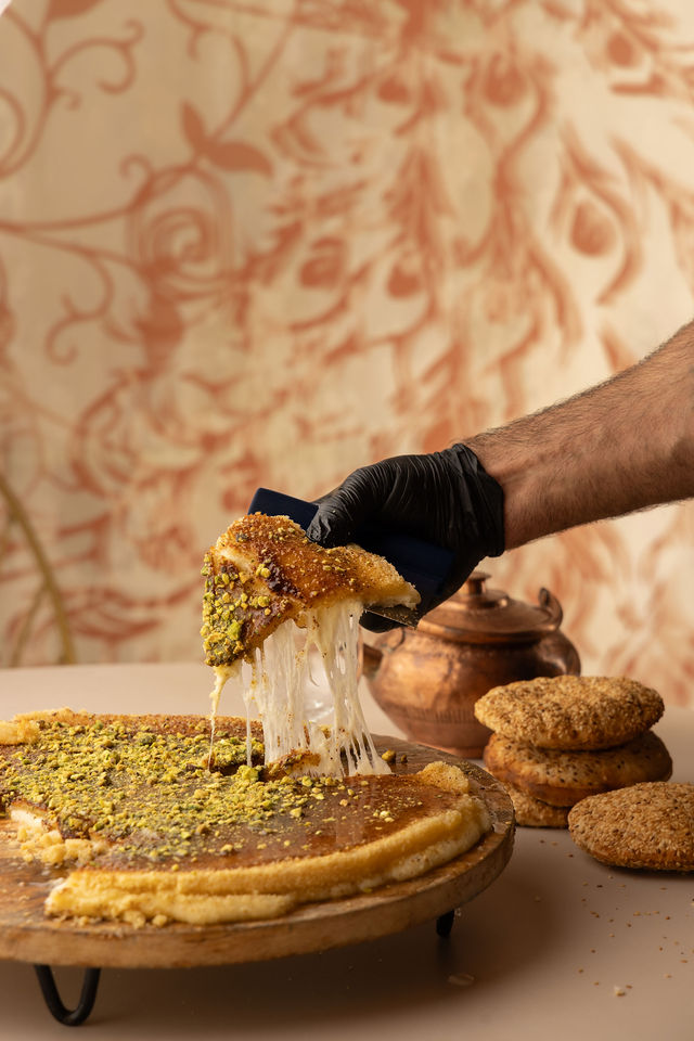 Part de knafeh fondant au fromage et pistache, servie à la main avec fond oriental