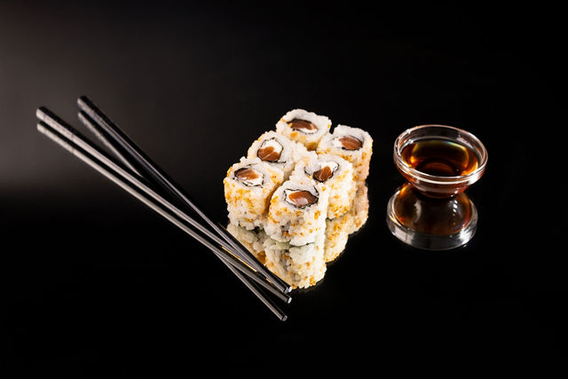 Sushi california avec sauce soja et baguettes noires sur fond noir brillant