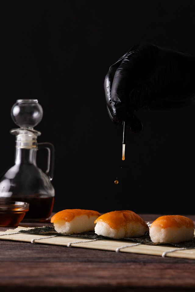 Geste culinaire versant de la sauce soja sur des sushis au saumon, fond noir