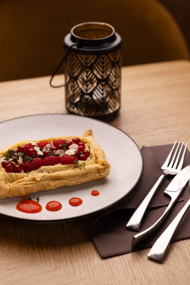 Tarte feuilletée garnie de framboises et groseilles, dressée avec coulis rouge