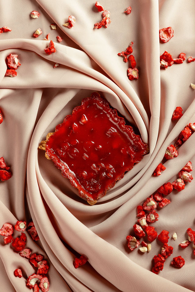 Tarte à la praline rose posée sur un tissu rose avec éclats de praline, stylisme gourmand