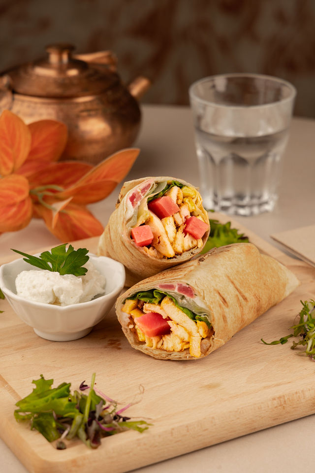 Wrap au poulet avec salade et crème, posé sur planche avec théière en cuivre