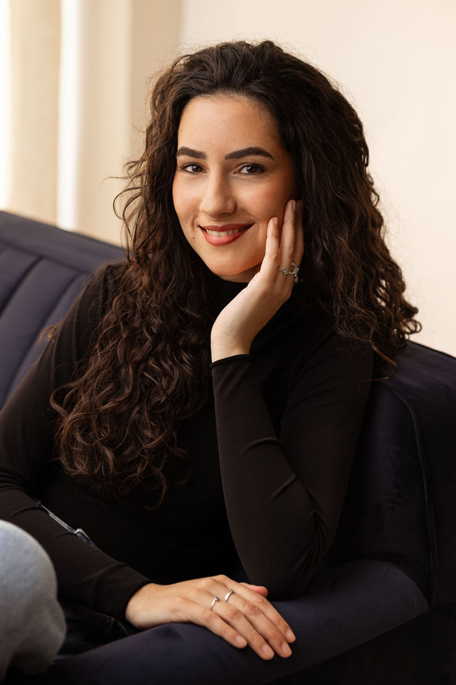 Portrait femme brune bouclée en haut noir, assise sur un fauteuil bleu