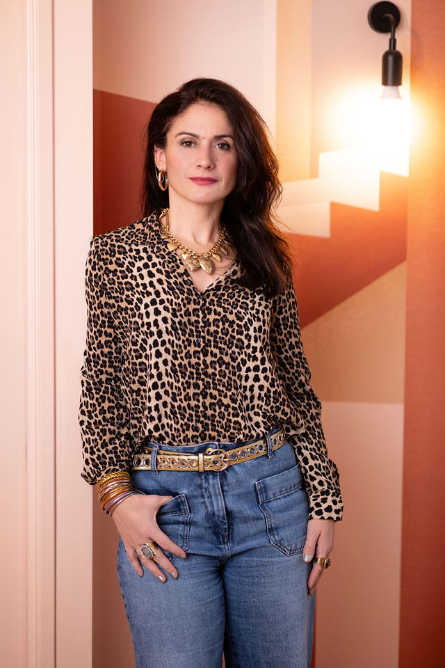 Portrait d’une femme en blouse léopard et jeans devant un mur coloré