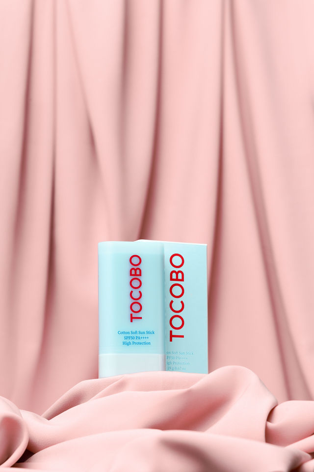 Stick solaire Tocobo bleu clair posé sur un tissu rose